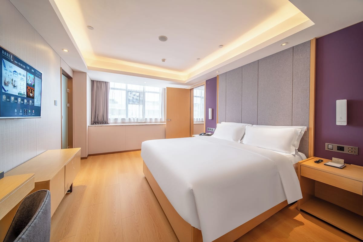 Quarto de hotel com uma cama grande, uma escrivaninha, uma TV e uma janela.