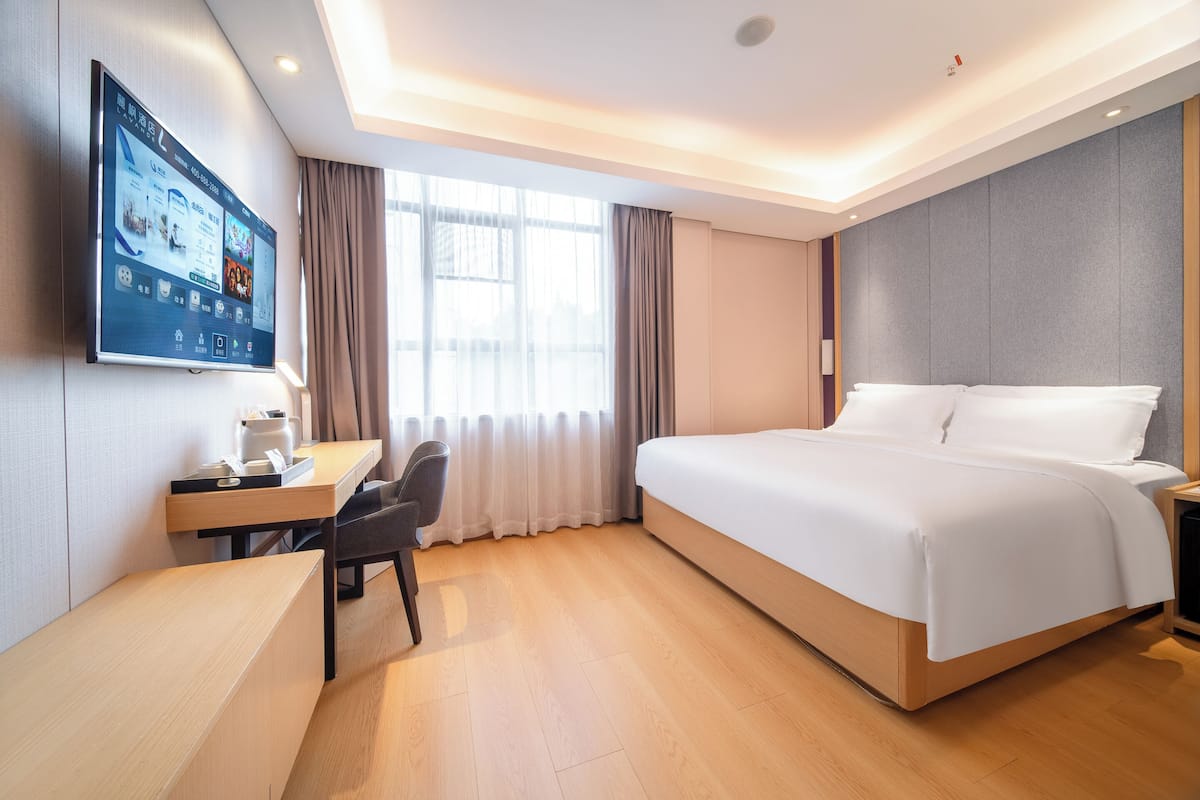 Una habitación de hotel con cama, escritorio, silla, televisor y cortinas.