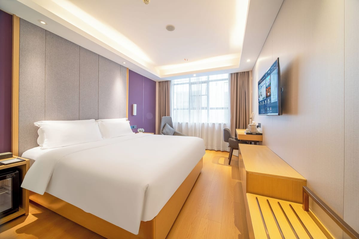 Quarto de hotel com uma cama grande, uma escrivaninha, uma cadeira, uma televisão e uma janela com cortinas.