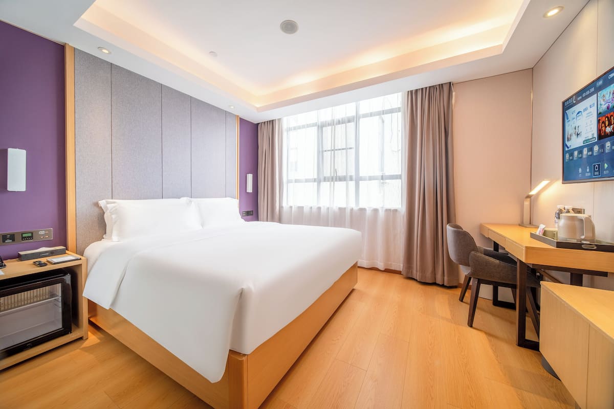 Quarto de hotel com cama, escrivaninha, cadeira e televisão fixada na parede.