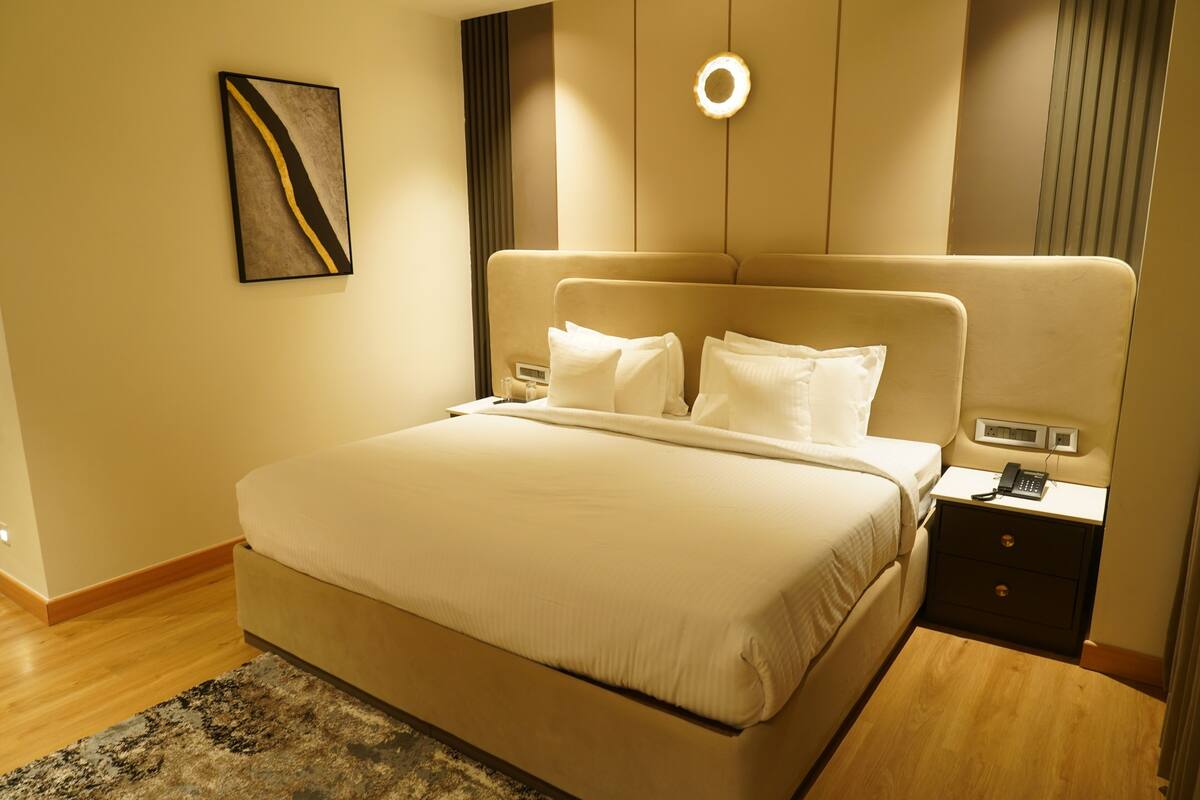 Ein Hotelzimmer mit einem großen Bett, Nachttischen, einer Wandleuchte und einem Gemälde.