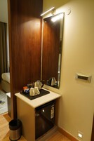 Un baño de hotel con puerta de madera, un lavabo con espejo, una toalla, un cesto de basura y un enchufe.