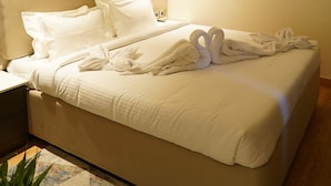 A neatly made bed with white linens and towels, a bedside table with a lamp, and a wall-mounted light fixture. - Luxe Manor (Kharar)