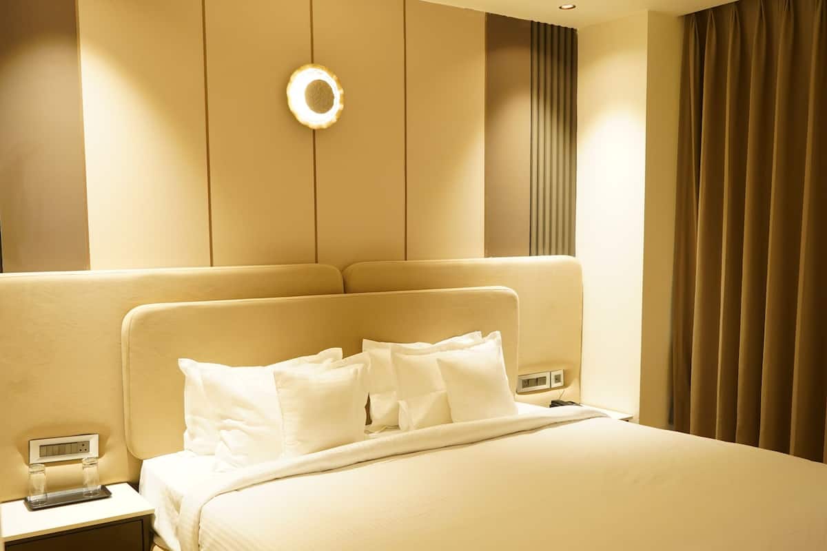Ein Hotelzimmer mit einem großen Bett, Nachttischen, einer Ablagefläche und einer Wandleuchte, sowie einem Fenster mit Vorhängen.