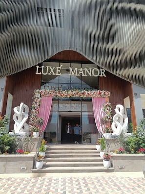 A building entrance with a sign reading 'LUXE MANOR,' featuring a modern design with vertical slats and a decorative archway. - Luxe Manor (Kharar)