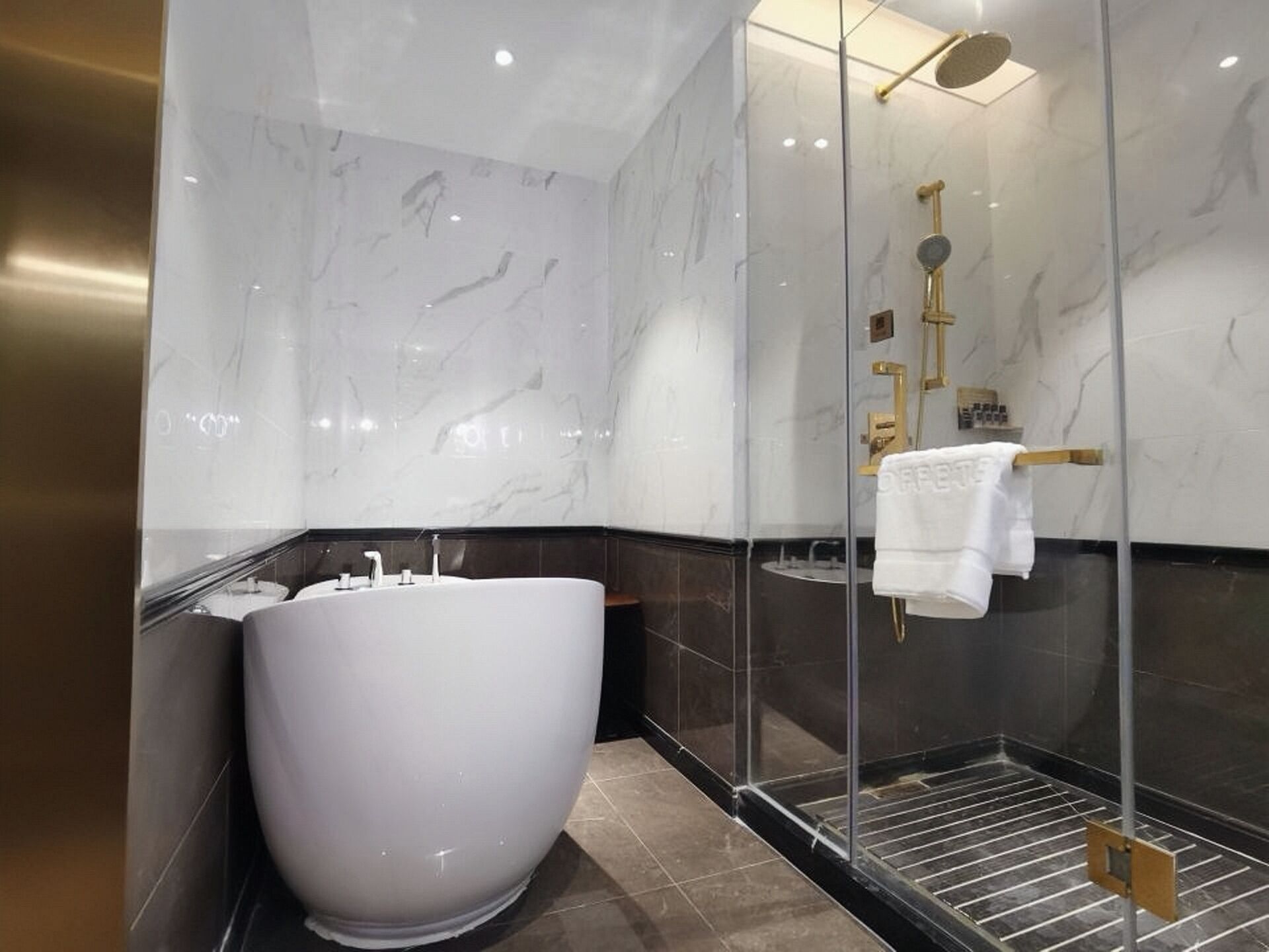 A modern bathroom with a large white bathtub, a glass-enclosed shower area, and a marble wall.
