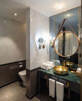 A modern bathroom with a marble wall, a toilet, a sink with a gold basin, and a large mirror with a copper frame.