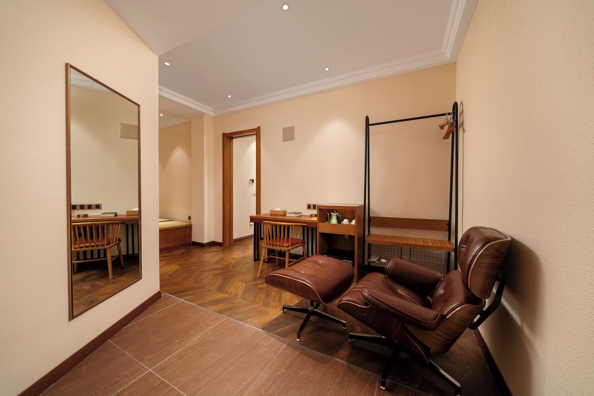 A hotel room with a large mirror, a wooden desk, a chair, and a massage chair.