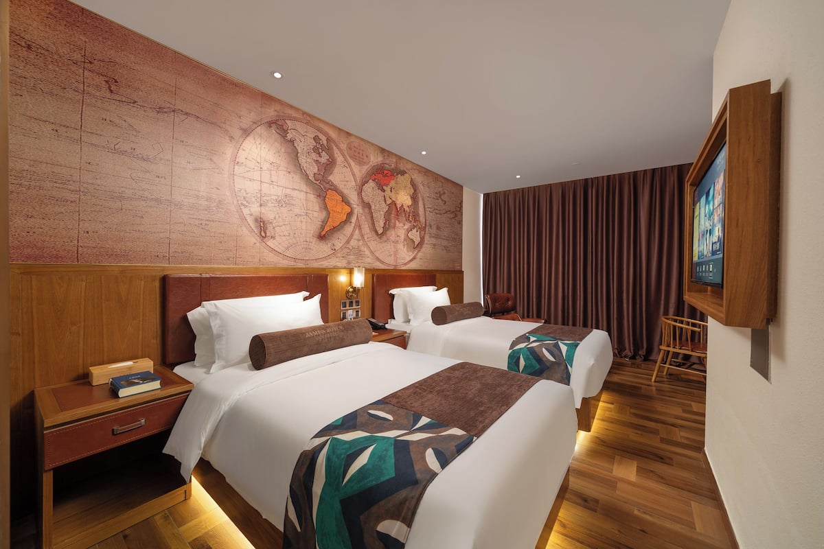 A hotel room with two beds, a wooden headboard, a world map on the wall, a TV, and a wooden floor.