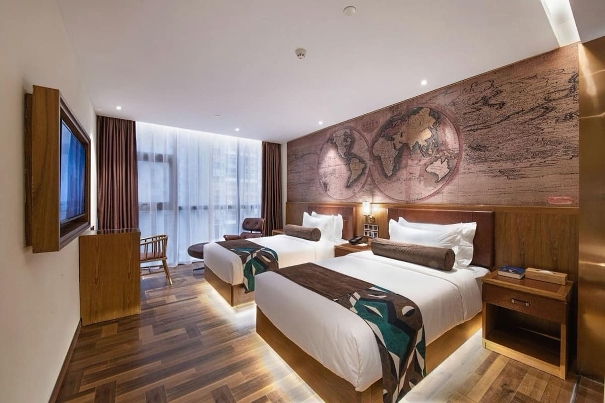 A hotel room with two beds, a large world map on the wall, a TV, and a wooden floor.