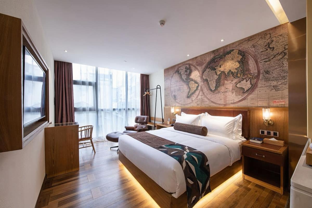 A hotel room with a large bed, a desk, a chair, a map on the wall, and a window with curtains.