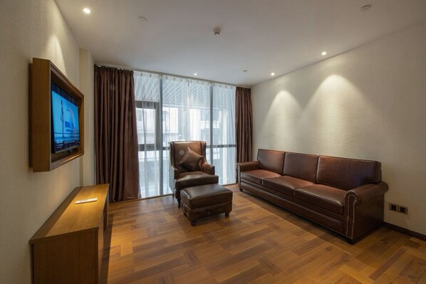 A modern living room with a leather sofa, a leather armchair, a wooden coffee table, and a flat-screen TV mounted on the wall. - ELITE James Joyce Coffetel Hotel Guangzhou Pedestrian Street Beijing Lu Metro Station Branch - Free Deliver Service to Canton Fair Complex During Canton Fair Period (Guangzhou)