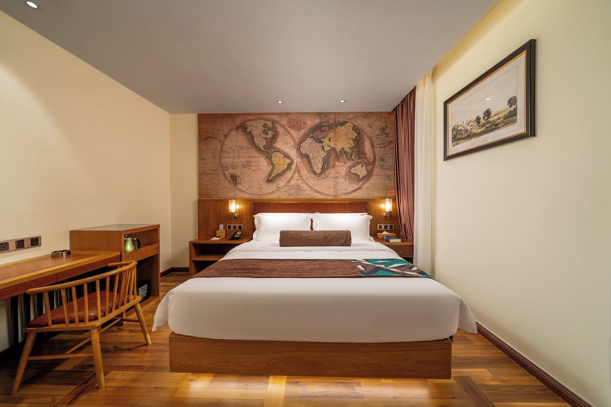 A hotel room with a large bed, a desk, a chair, a map on the wall, and a framed picture.
