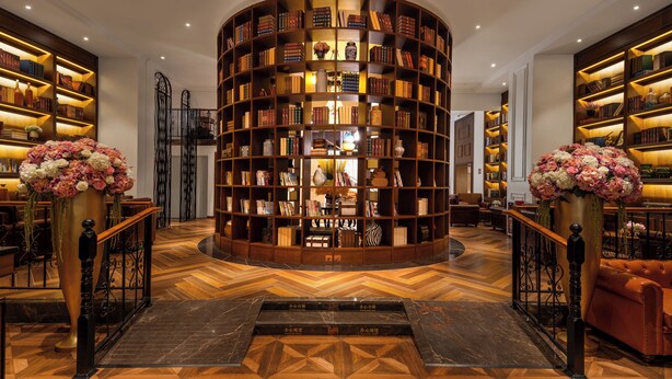 A circular bookshelf with books, a central table, and two large vases with flowers. - ELITE James Joyce Coffetel Hotel Guangzhou Pedestrian Street Beijing Lu Metro Station Branch - Free Deliver Service to Canton Fair Complex During Canton Fair Period (Guangzhou)