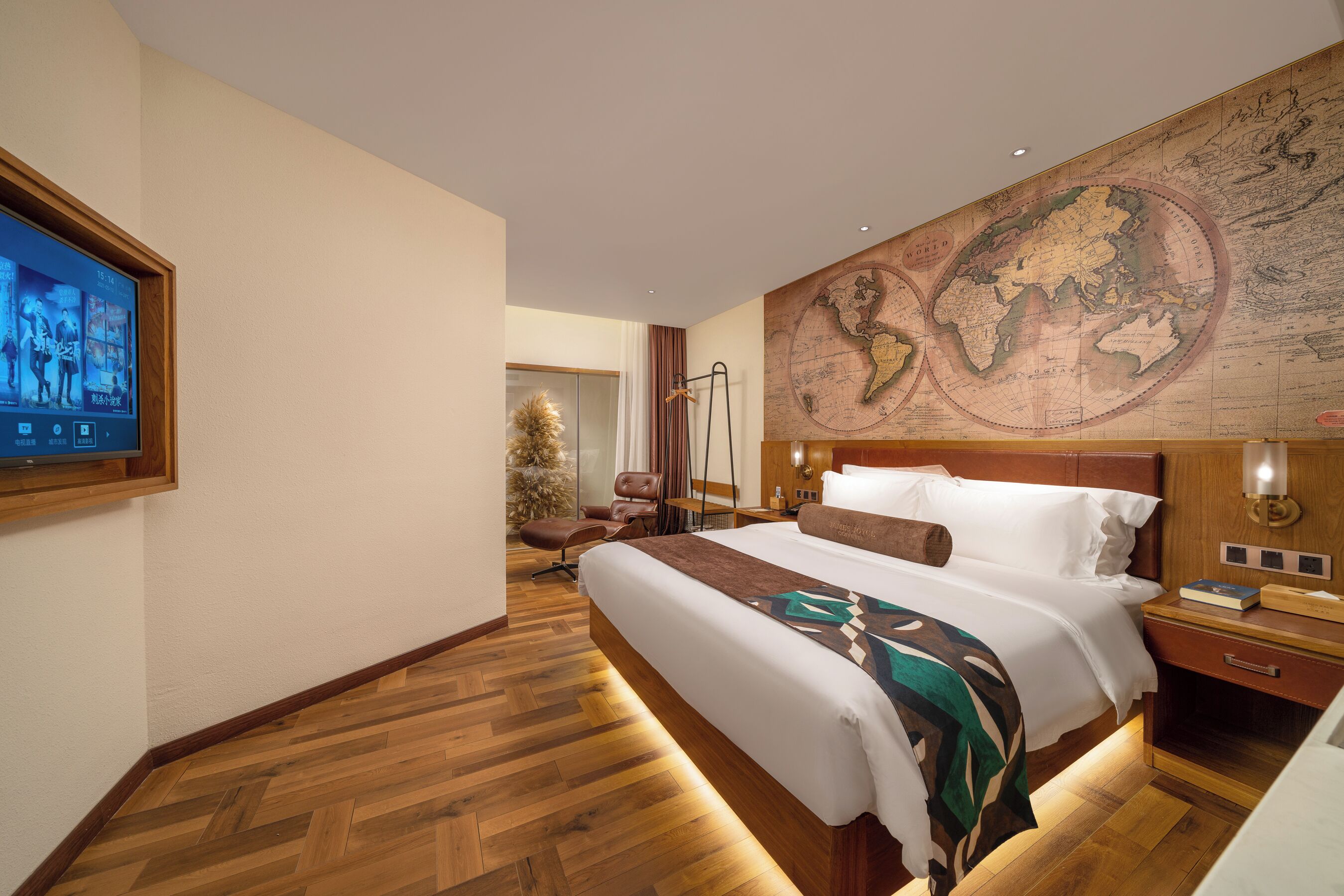 Une chambre d’hôtel avec un grand lit, un plancher en bois, une carte du monde accrochée au mur, un téléviseur fixé au mur et une table de chevet avec une lampe.