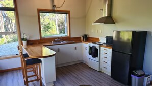 Eine kompakte Küche mit Holztischplatte, weißen Schränken, einem Edelstahlkühlschrank und einem Fenster mit Blick auf Grünflächen.