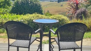 Eine überdachte Terrasse mit zwei Stühlen und einem Tisch, mit Blick auf eine schöne Landschaft.