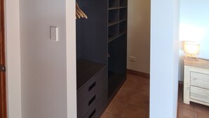 Ein Zimmer mit Holzboden, einem Schrank mit Regalen, einem Bett und einem Nachttisch mit Lampe.