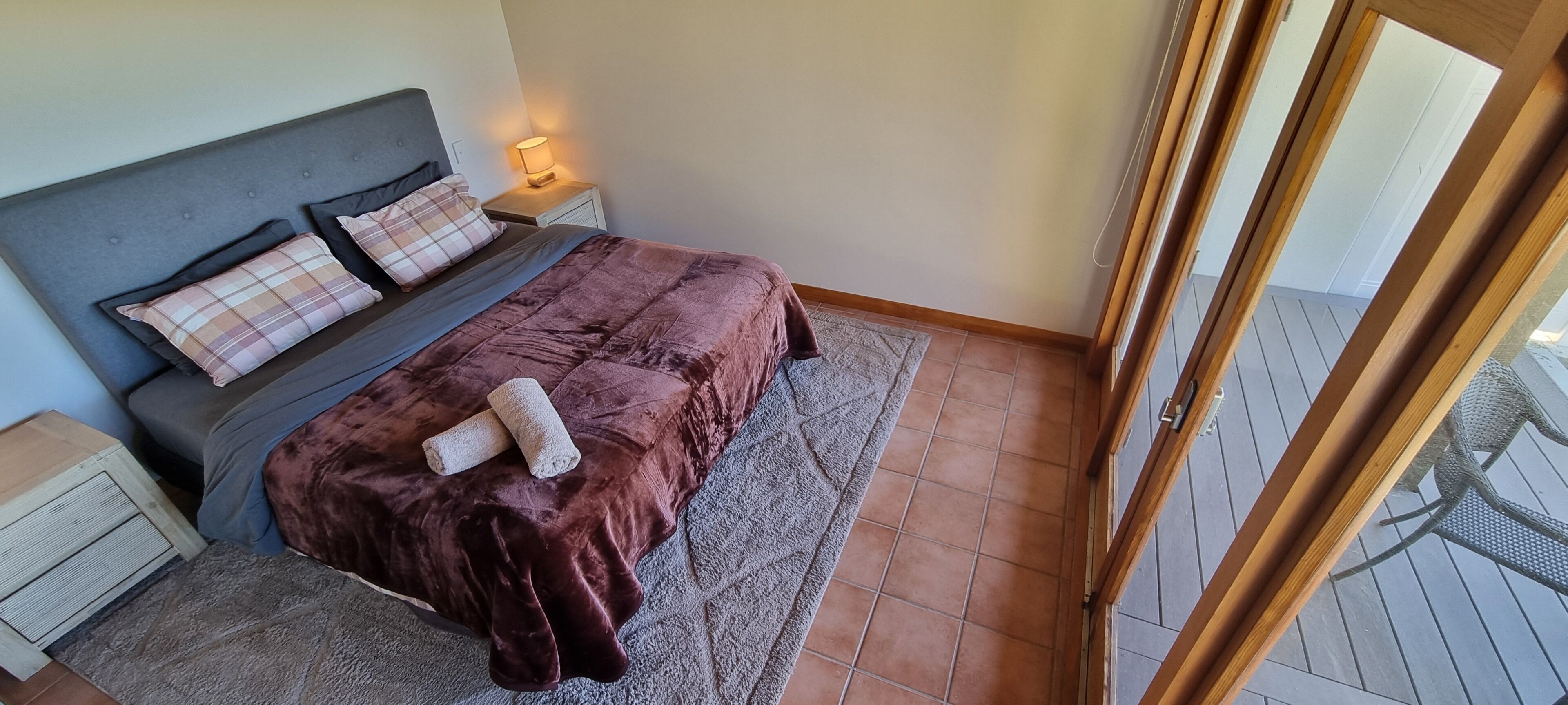 Ein Schlafzimmer mit Bett, Nachttischen, einer Lampe und Blick ins Freie.