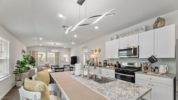 A modern kitchen with white cabinetry, a large island with a sink, and stainless steel appliances. - Brand-New Home - Near Fort Sam & Randolph - Safe (Converse)
