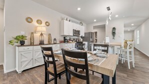 A modern kitchen with white cabinetry, a microwave, and a refrigerator. There is a dining area with a wooden table and chairs. - Brand-New Home - Near Fort Sam & Randolph - Safe (Converse)