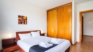 Una camera d'hotel con un letto in legno, biancheria bianca, un comodino, un quadro appeso al muro e un armadio in legno.
