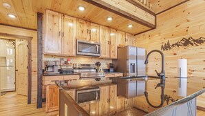 Interno di una baita in legno con cucina, caratterizzata da mobili in legno, elettrodomestici in acciaio inossidabile e un piano di lavoro in granito.