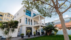 Una casa moderna de dos pisos con un balcón, césped cuidado y vegetación circundante.