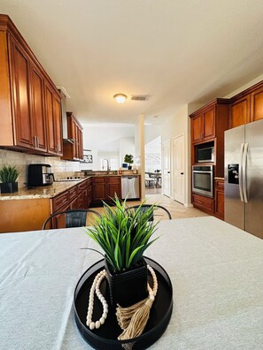 A modern kitchen with wooden cabinets, a stainless steel refrigerator, and a dining area with a table and chairs. - Charming 3-bedroom house in Houston perfect for your getaway (Houston)