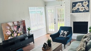 Ein Wohnzimmer mit Kamin, Deckenventilator und großem Fenster mit Jalousien.