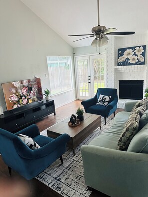 A living room with a fireplace, a ceiling fan, and a large window with blinds. - Charming 3-bedroom house in Houston perfect for your getaway (Houston)