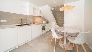 A modern kitchen with white cabinetry, a built-in oven, and a dining area with a round table and white chairs. - GuestReady - Charming duplex in the Alfama heart (Lisbon)