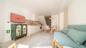 A modern living room with a sofa, a TV mounted on the wall, a kitchen area with a staircase, and a green cabinet with a floral design. - GuestReady - Charming duplex in the Alfama heart (Lisbon)