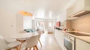 A modern kitchen with white cabinetry, a built-in oven, and a dining area with a round table and chairs. - GuestReady - Charming duplex in the Alfama heart (Lisbon)