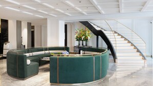 A spacious living area with a curved green sofa, a coffee table, and a staircase with a black railing. - XANA Deluxe International Hotel Guangzhou East Railway Station Branch - Free Shuttle Bus to Canton Fair Complex During Canton Fair Period (Guangzhou)