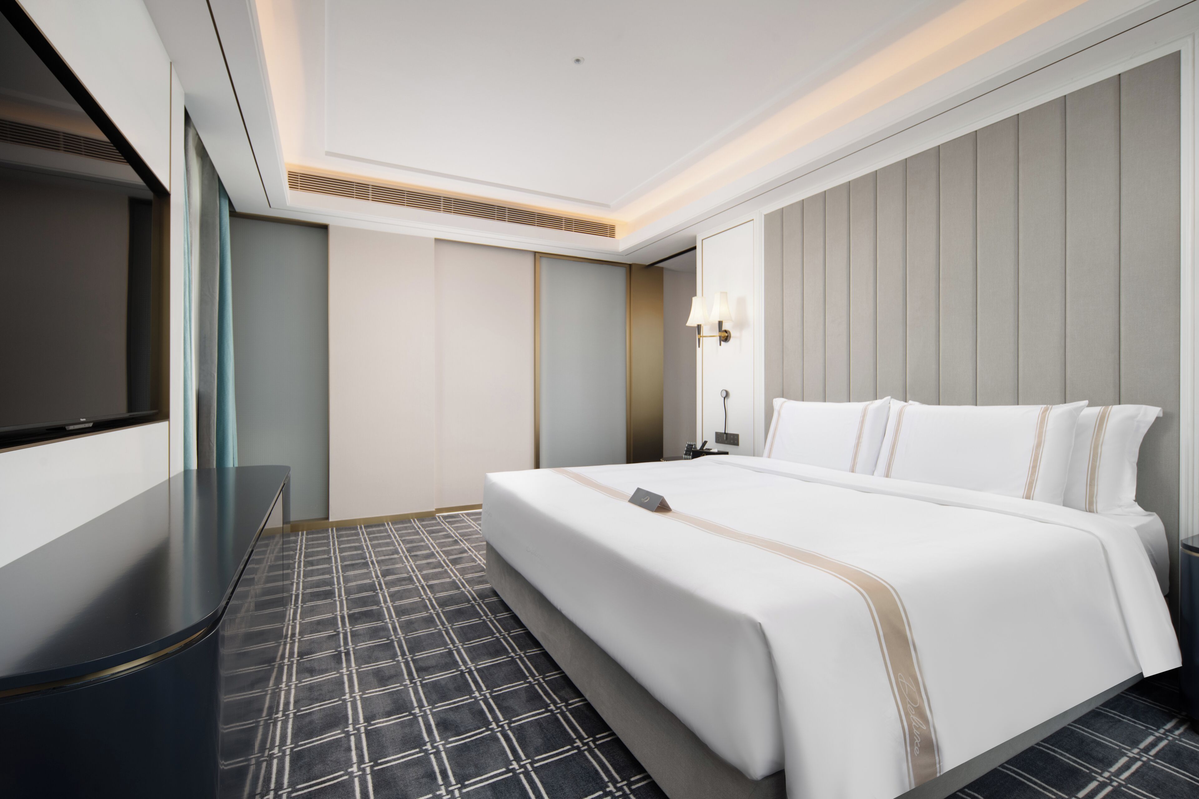 Habitación de hotel con cama, televisor, escritorio y alfombra estampada.