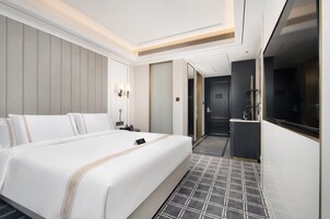 A hotel room with a large bed, a small desk, a mirror, a wardrobe, and a television.