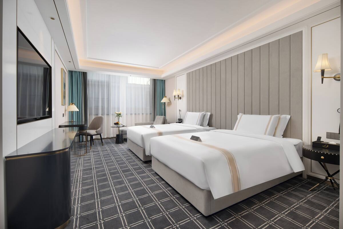 A hotel room with two beds, a desk, a chair, a TV, and a window with curtains.