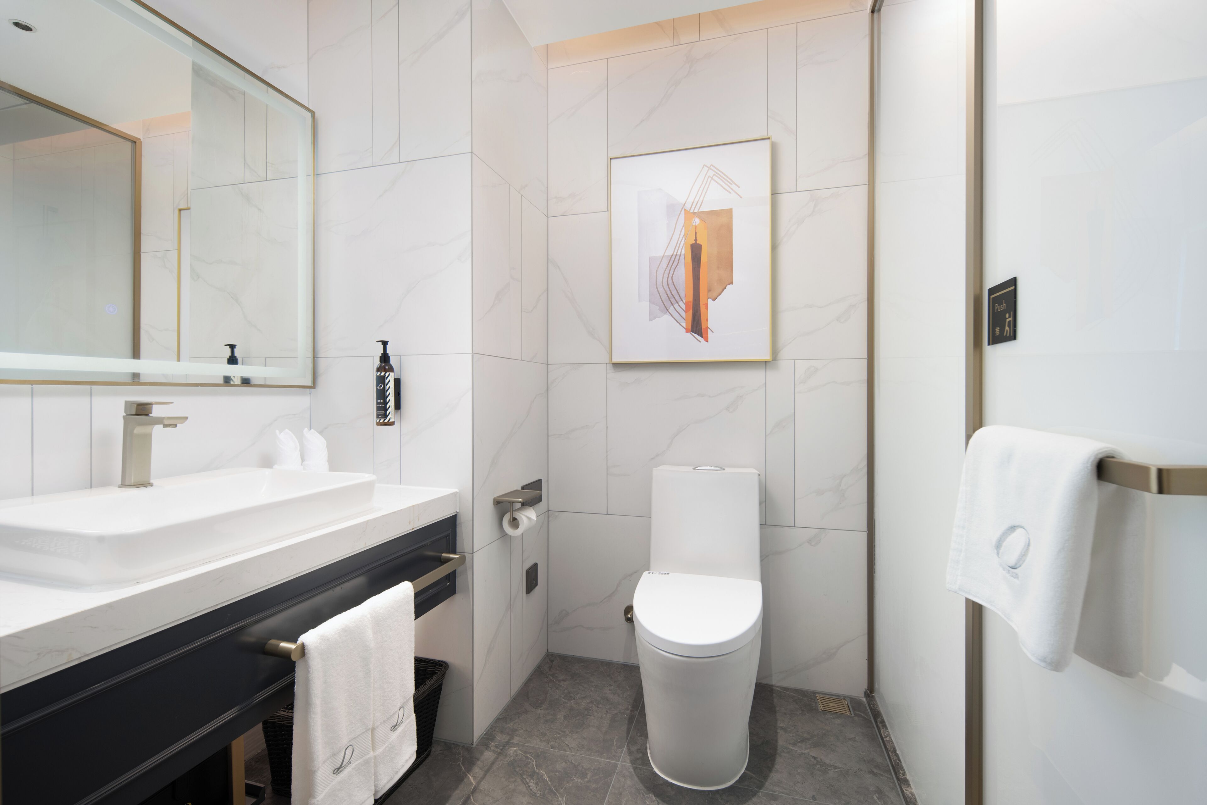 Un baño moderno con un espejo grande, un inodoro, un lavamanos y un dispensador de toallas.