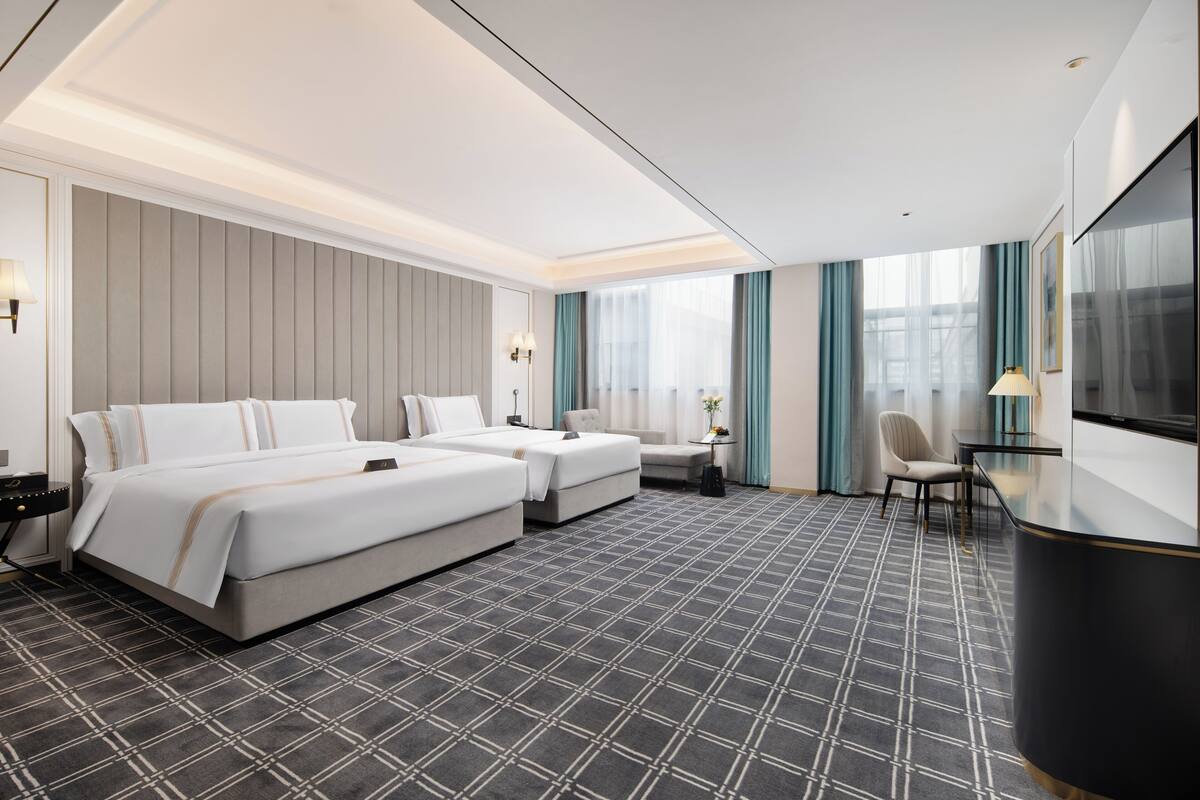 A hotel room with a large bed, a smaller bed, a desk, and a TV.