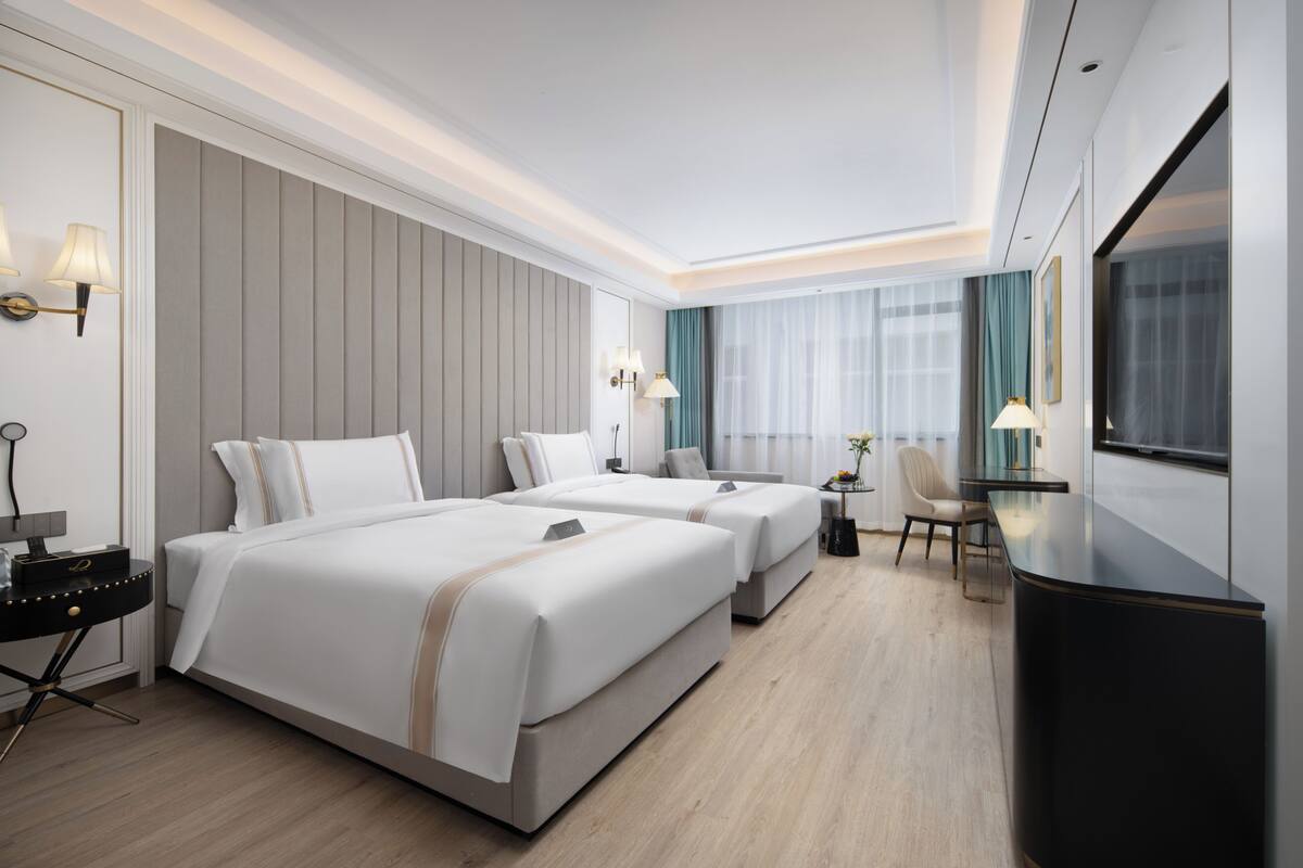 A hotel room with two beds, a desk, a chair, and a television.