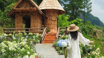 A wooden structure with a conical roof, surrounded by a garden with various flowers and a staircase leading up to it.