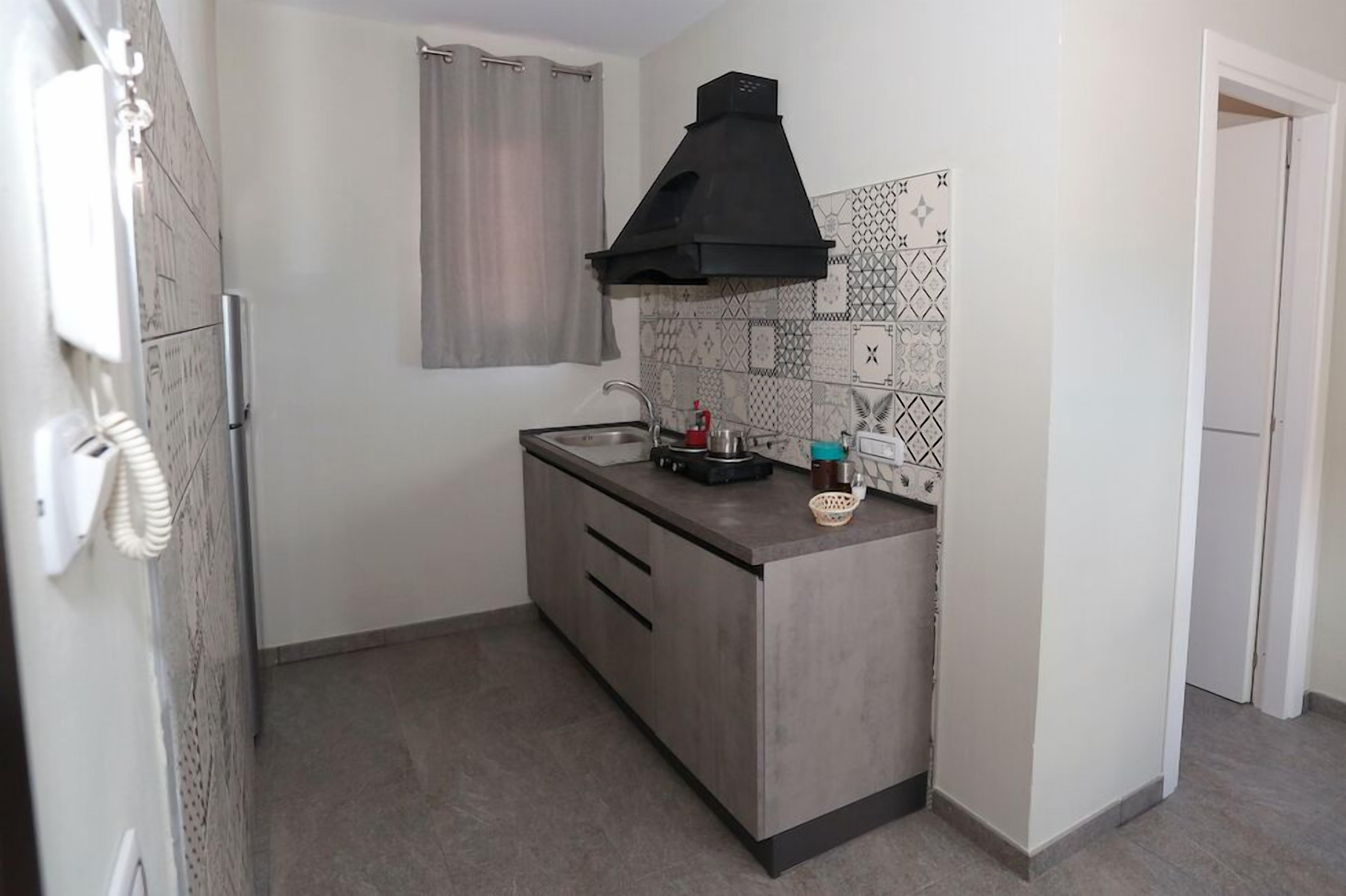 A compact kitchen with a modern design, featuring a grey countertop, a black range hood, and patterned backsplash tiles.