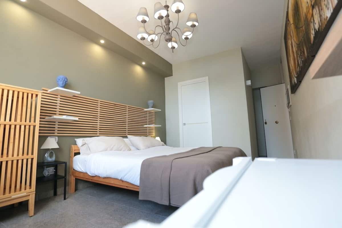 A bedroom with a bed, bedside tables, a wooden slat headboard, a chandelier, and a door.