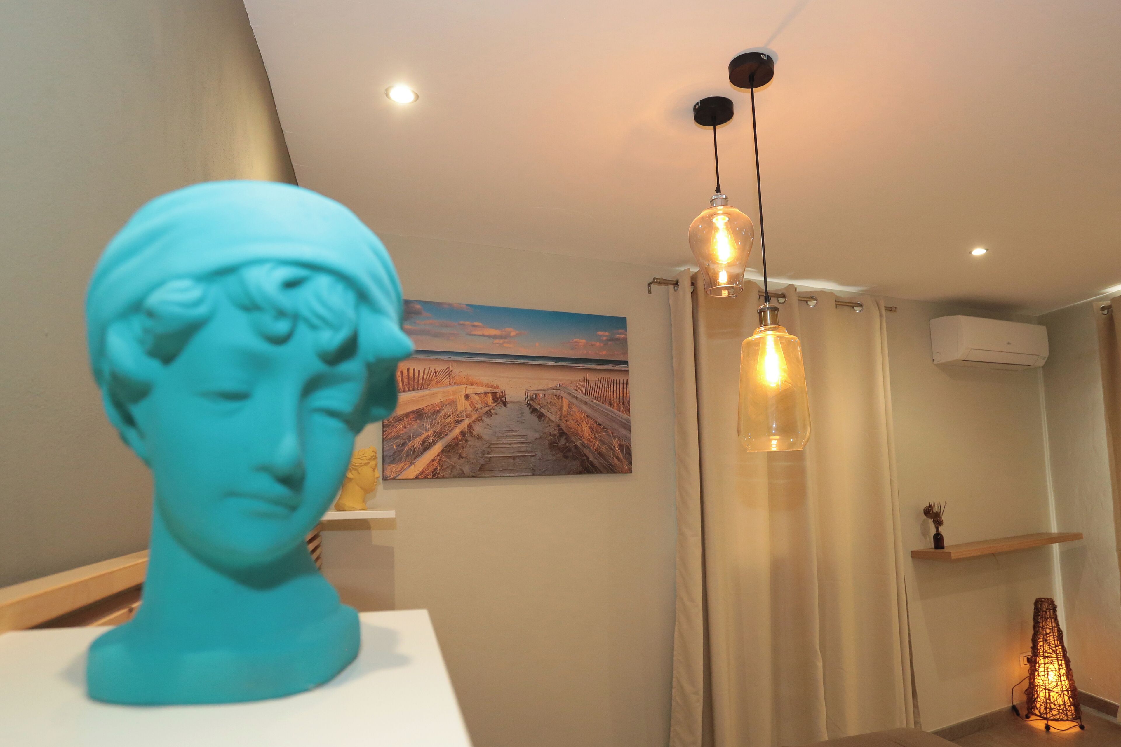 A room with a bust sculpture, a painting of a bridge, a hanging light fixture, and an air conditioning unit.
