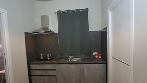 Pieni, käytännöllinen keittiö, jossa on pesuallas, kaappeja, liesi ja ikkuna, jossa on verho.