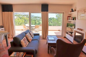 Ein Wohnzimmer mit Sofa, Couchtisch, Fernseher und einem Balkon mit Aussicht.