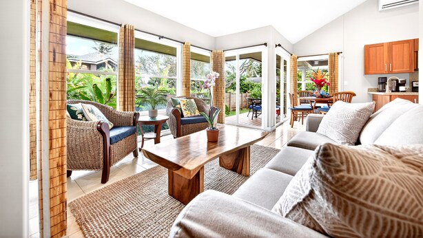 Un vaste espace de vie comprenant un canapé, une table basse et une table à manger, de grandes fenêtres avec des rideaux et un ventilateur de plafond.