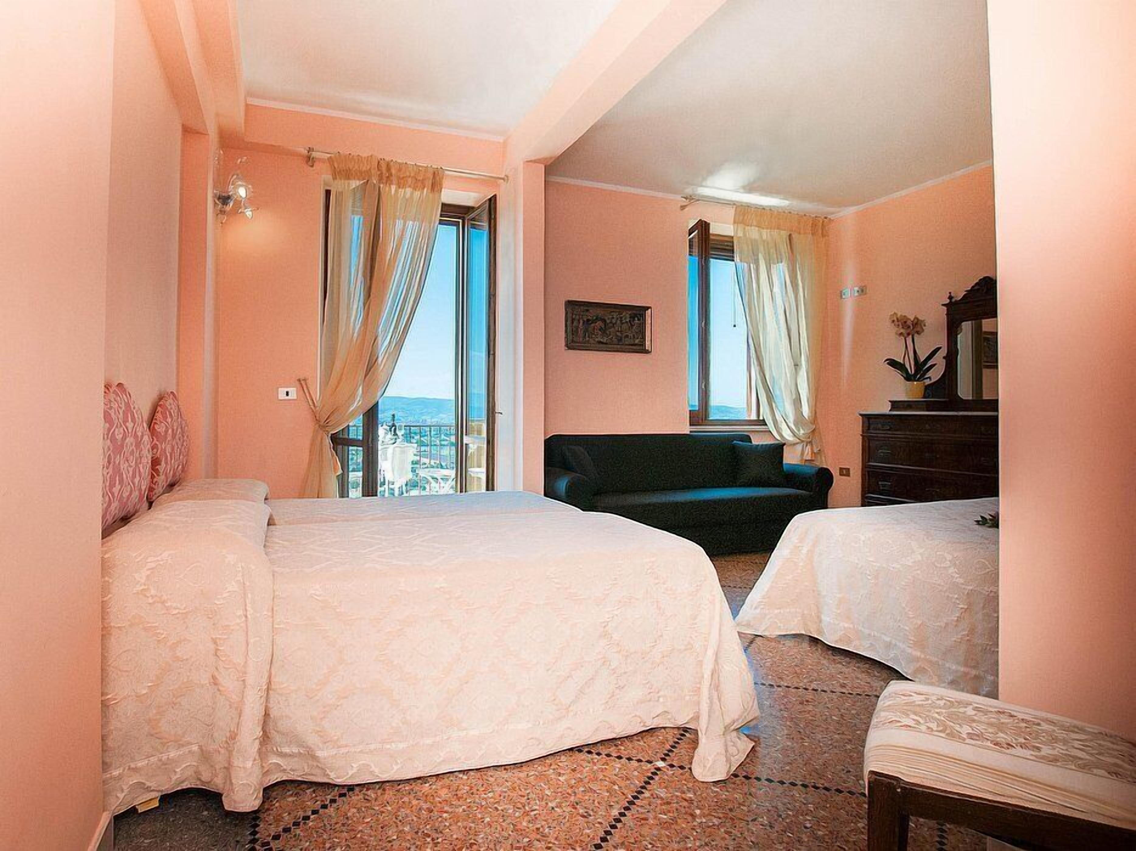 A hotel room with two beds, a sofa, a dresser, and a view of the city.