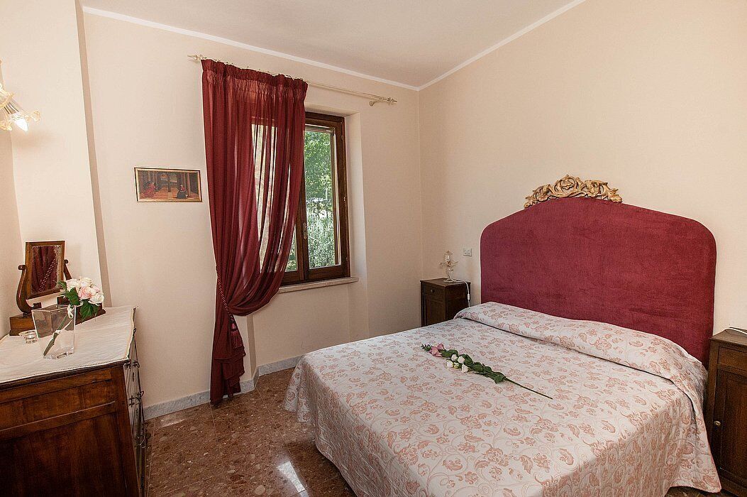 Une chambre à coucher comprenant un lit, une table de chevet, une commode, une fenêtre avec des rideaux et un tableau encadré accroché au mur.